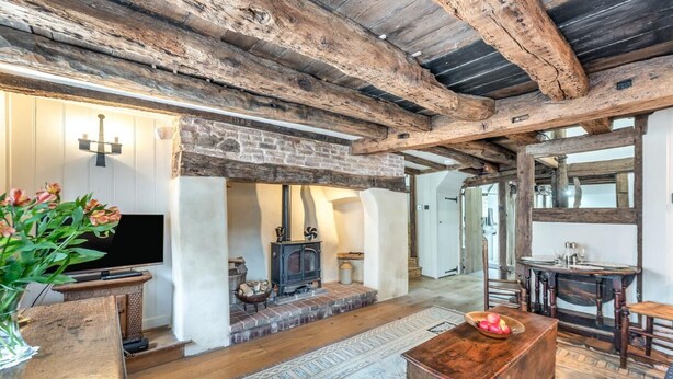 A rustic interior with exposed wooden beams, a stone fireplace, a television, and a dining area with a wooden table and chairs. - 2 Bed in Battle (oc-f32643) (Battle)
