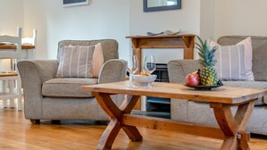 Una sala de estar con dos sofás grises, una mesa de centro de madera y una pequeña mesa de madera con una piña y un cuenco.
