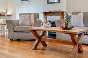 A living room with two grey sofas, a wooden coffee table, and a small wooden table with a pineapple and a bowl. - 3 Bed in Padstow (oc-p00175) (Padstow)