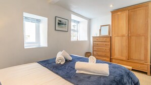 Un dormitorio con una cama, dos ventanas, un tocador y un armario.