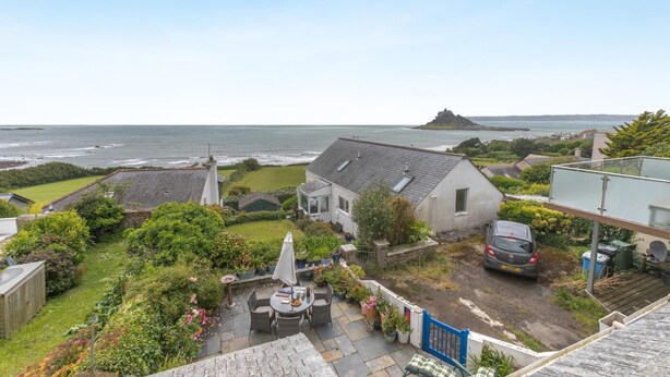 Una zona residencial costera con una casa, muebles de patio y vistas al mar.