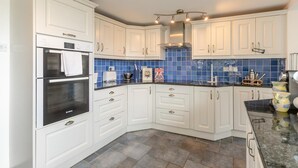 Una cocina con armarios blancos, horno Bosch, azulejos de salpicadero azules y encimera de granito.