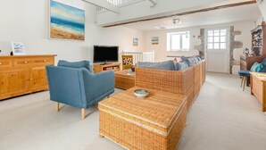 Un salón amplio con televisor, muebles de mimbre y un techo alto con vigas a la vista.