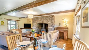 A cozy living room with a stone fireplace, wooden beams, a sofa, and a dining table set for a meal. - 2 Bed in Cantref (oc-t32629) (Cantref)