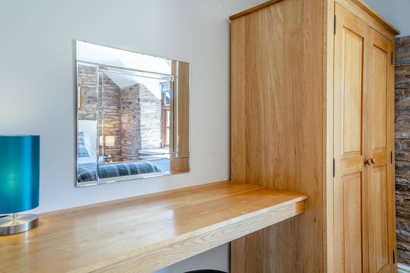 A wooden cabinet with a mirror above it, a wooden countertop, and a stone wall in the background.