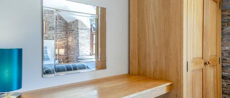 A wooden cabinet with a mirror above it, a wooden countertop, and a stone wall in the background.