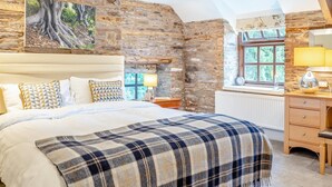 A bedroom with a large bed, a wooden dresser, a nightstand, and a stone wall. - 2 Bed in Cantref (oc-t32629) (Cantref)