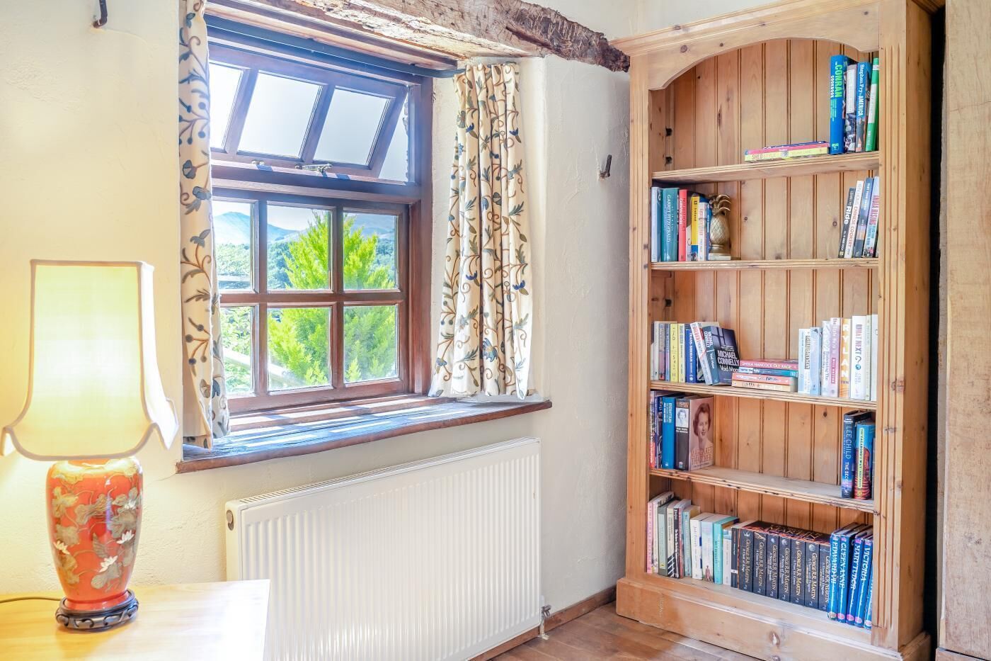 A room with a wooden bookshelf, a window with curtains, and a radiator.