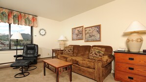 A living room with a leather chair, a brown sofa with patterned cushions, a wooden coffee table, a lamp, a clock, and two framed pictures on the wall. - Spacious Studio on Keystone Lake with Full Kitchen (Keystone)