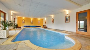 A large indoor swimming pool with a blue water feature, surrounded by stone flooring and yellow walls. - 2 Bed in Hemblington (oc-2134) (Hemblington)