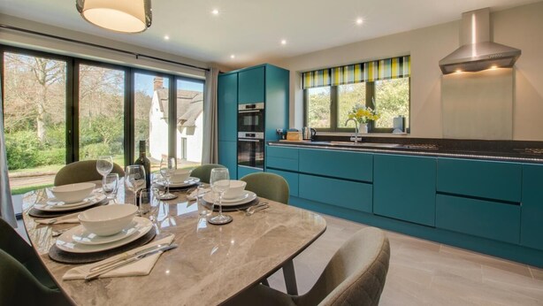 A modern kitchen with teal cabinetry, a marble countertop, and a large window overlooking a garden. - 2 Bed in Hemblington (oc-2134) (Hemblington)