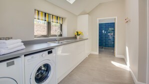 A modern kitchen with a built-in washing machine, a window with a striped blind, and a blue-tiled backsplash. - 2 Bed in Hemblington (oc-2134) (Hemblington)