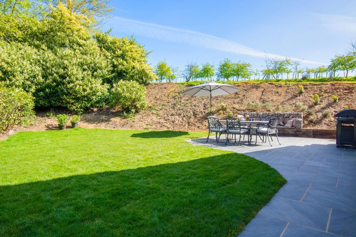 A patio area with a table and chairs, a barbecue grill, and a well-maintained lawn.
