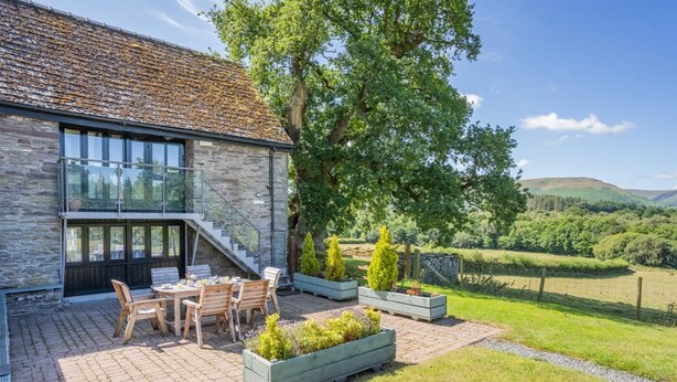 Une maison moderne avec une façade en pierre, un escalier en verre et un patio agrémenté de mobilier d’extérieur.
