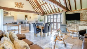Un vaste espace de vie doté d’un plafond haut, de poutres apparentes en bois, d’un coin repas avec des meubles modernes et d’une cheminée en pierre.