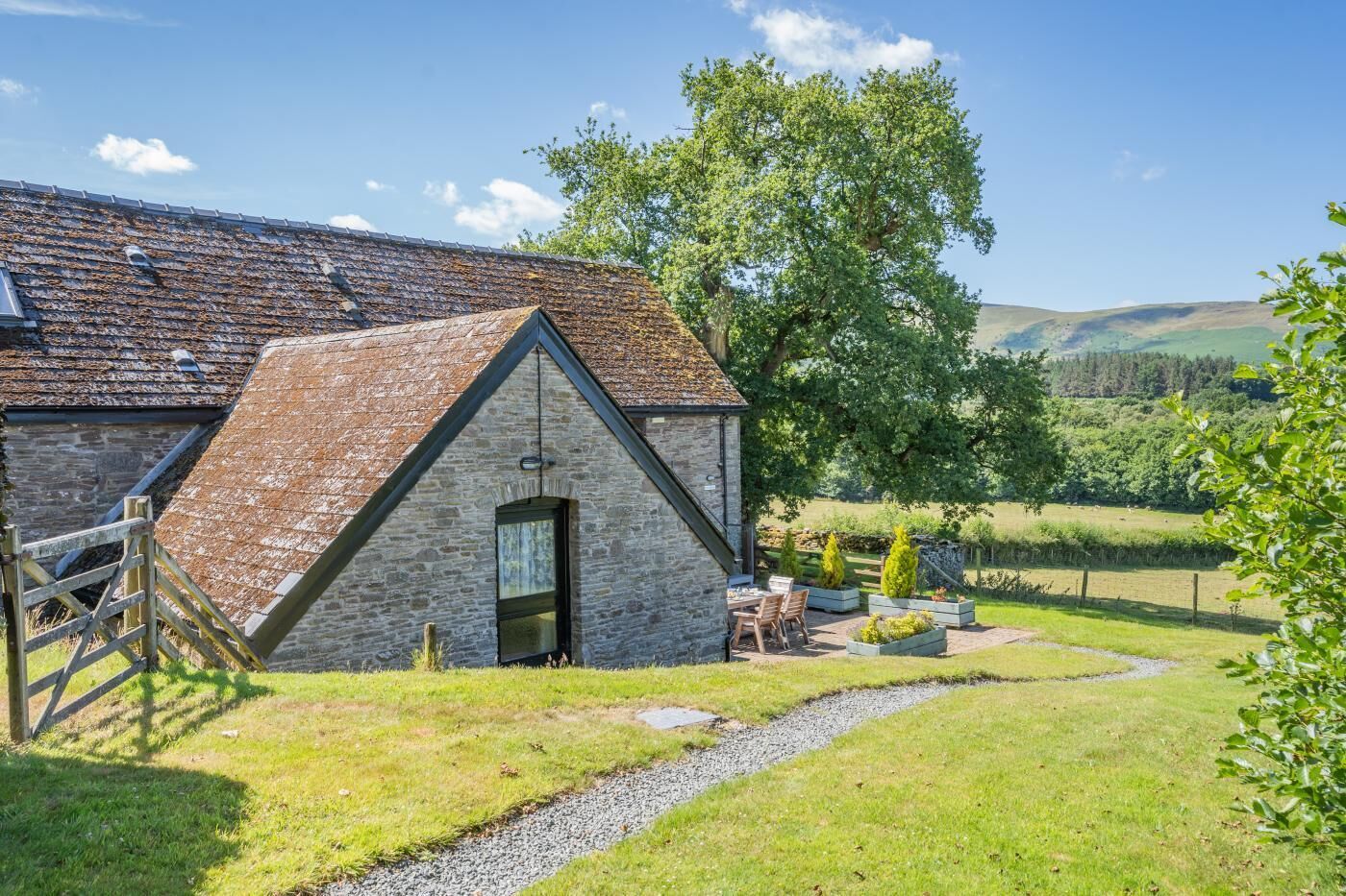 A stone building with a sloped roof, a wooden door, and a small patio with outdoor seating.