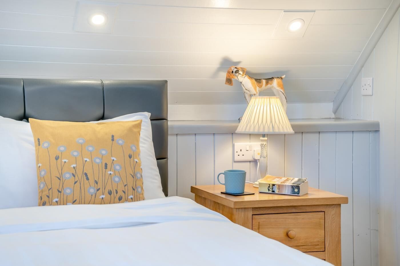 Ein Schlafzimmer mit einem Bett, einem Nachttisch, einer Lampe, einer blauen Tasse und einer Zeitschrift.