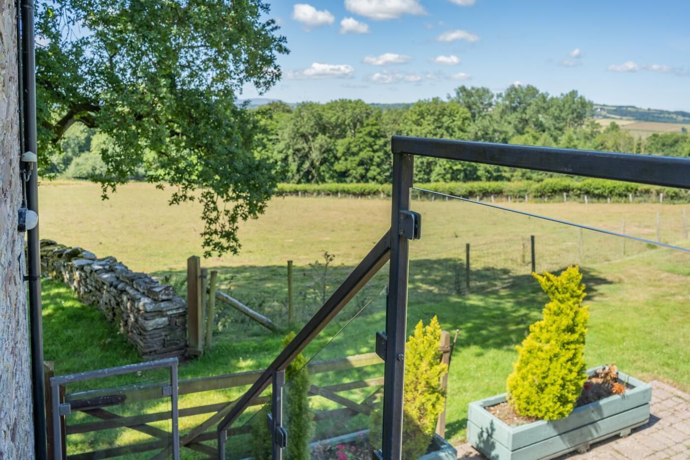 A view from a balcony overlooking a grassy field with a stone wall and a wooden fence.