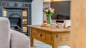 Uma sala de estar aconchegante com lareira, uma mesa de centro de madeira com um vaso de flores e uma televisão.