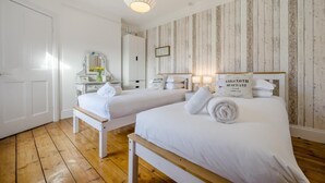Quarto de hotel com duas camas, soalho de madeira, paredes brancas, um painel de parede em madeira, um espelho, uma cômoda e um candeeiro pendente.