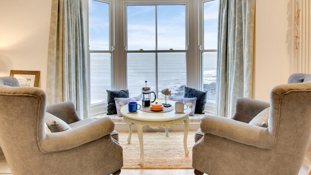 Et hjørneværelse med karnap, havudsigt, to lænestole, et lille rundt bord med kaffe, og udsigt over havet.