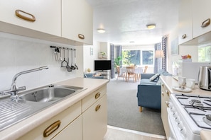 A modern kitchen with stainless steel appliances, a dining area with a TV, and a cozy seating area with a sofa and table. - 2 Bed in Lynton (oc-p13830) (Barbrook)