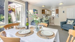 A dining area with a table set for four, a bottle of champagne, and a vase with flowers. - 2 Bed in Lynton (oc-p13830) (Barbrook)