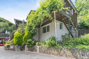 A two-story building with a stone wall and a wooden staircase leading to the upper floor. - 2 Bed in Lynton (oc-p13830) (Barbrook)