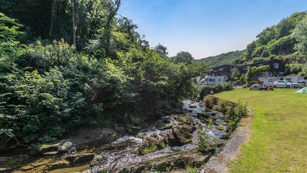 A natural setting with a stream, lush greenery, and a row of houses with a clear view of the landscape. - 2 Bed in Lynton (oc-p13830) (Barbrook)