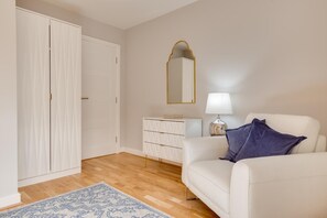 A room with a white wardrobe, a white dresser, a white sofa with a blue pillow, a mirror, and a lamp. - 4 Bed in Seahouses (oc-gd1916) (Seahouses)