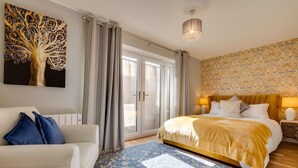 A bedroom with a bed, a sofa, a chandelier, and a large window with curtains. - 4 Bed in Seahouses (oc-gd1916) (Seahouses)