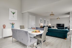 Un salon moderne avec un canapé de couleur turquoise, un coin repas doté d’une table blanche et un téléviseur en arrière-plan.