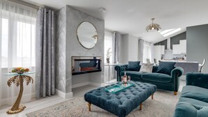 A modern living room with a TV, dark blue sofas, a glass coffee table, and a patterned rug. - 4 Bed in Seahouses (oc-gd1916) (Seahouses)