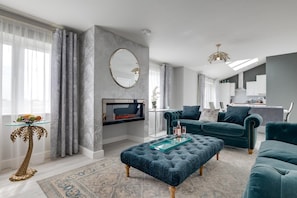 Un salon moderne avec un téléviseur, des canapés bleu foncé, une table basse en verre et un tapis à motifs.