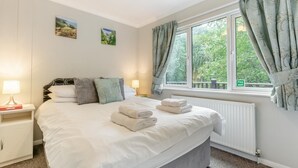 A neatly made bed with pillows and folded towels, a bedside table with a lamp, and a window with curtains. - 2 Bed in Lynton (oc-r13823) (Barbrook)