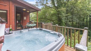 A hot tub on a wooden deck with a table and chairs, surrounded by a wooden fence and trees. - 2 Bed in Lynton (oc-r13823) (Barbrook)