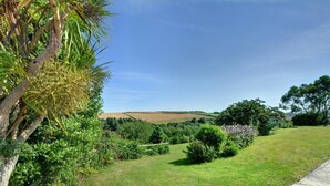 A grassy landscape with a clear sky, trees, and a distant view of rolling hills. - 1 Bed in Wadebridge (oc-p00440) (Saint Issey)