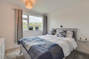 Ein Schlafzimmer mit Bett, Nachttisch, Fenster mit Vorhängen und Blick nach draußen.