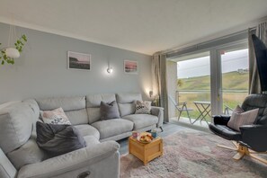Ein Wohnzimmer mit grauem Sofa, einem Holztisch und einem schwarzen Sessel.