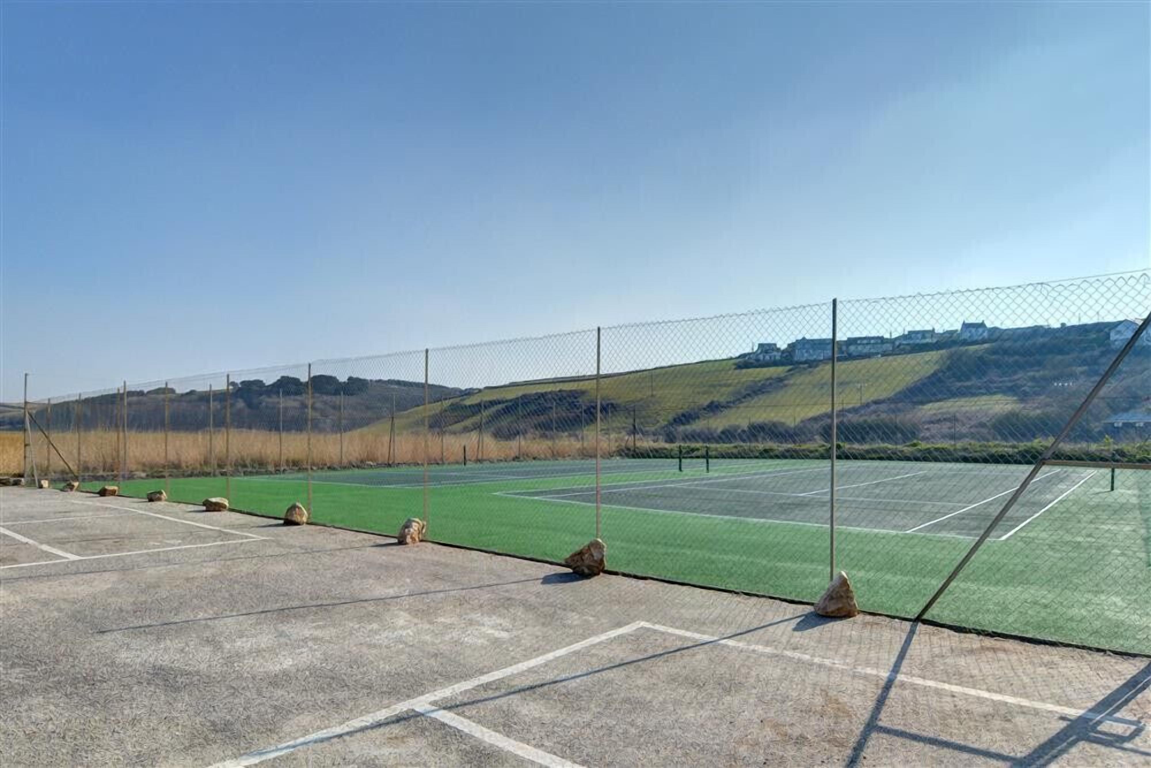 A tennis court with a chain-link fence, surrounded by a hilly landscape.