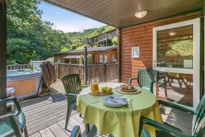 Eine Holzterrasse mit einem für zwei Personen gedecktem Tisch, einem Whirlpool und einer Holzhütte im Hintergrund.