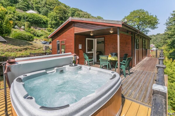 Eine Holzhütte mit Whirlpool und Sitzgelegenheit im Freien, umgeben von viel Grün.