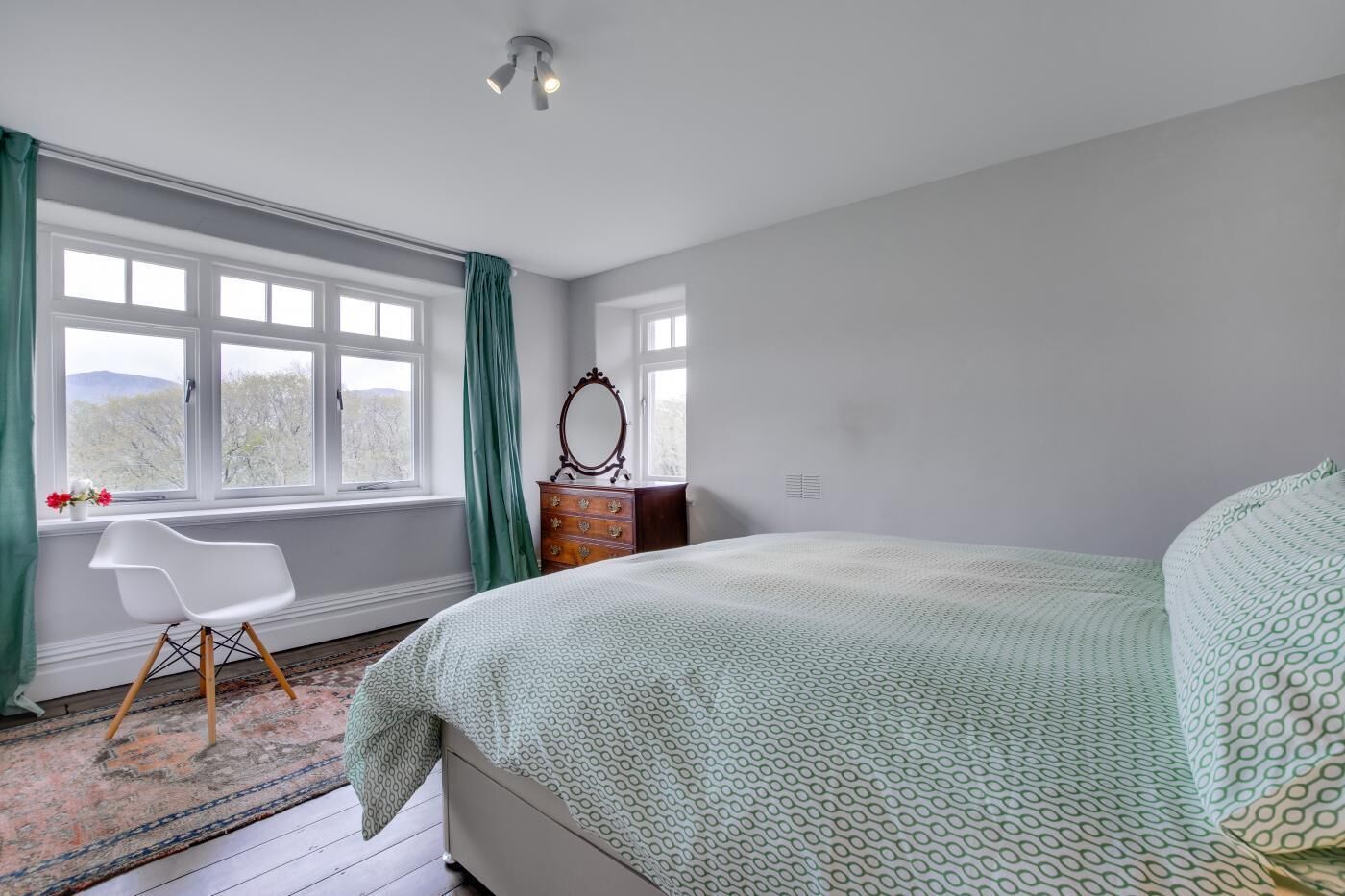 Ein Schlafzimmer mit Bett, Schminktisch, Stuhl und einem Fenster mit Vorhängen.