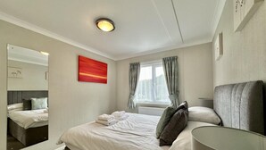 Ein Hotelzimmer mit einem großen Bett, einem Nachttisch, einem Spiegel, einem Fenster mit Vorhängen und einem roten Gemälde an der Wand.