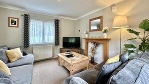 Ein Wohnzimmer mit einem grauen Sofa, einem Holztisch, einem Fernseher, einem Kamin und einer großen Pflanze.