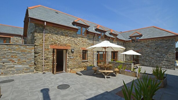 A stone building with a patio area featuring outdoor seating and umbrellas. - 2 Bed in Padstow (oc-p00282) (Porthcothan Bay)