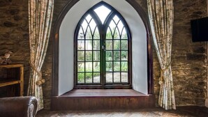 Une pièce dotée d’une grande fenêtre en arc de cercle, de murs en pierre et d’un banc en bois.