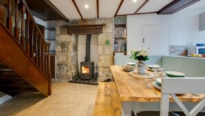 Un intérieur chaleureux avec une cheminée en pierre, un escalier en bois et un coin repas où une table est dressée pour deux personnes.