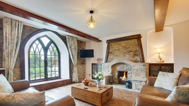 Un salon chaleureux avec une cheminée en pierre, des meubles en bois et une grande fenêtre en arc de cercle.