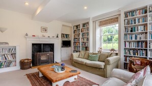 Ein gemütliches Wohnzimmer mit Kamin, einer Couch, einem Couchtisch und einem Bücherregal voller Bücher.